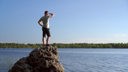 A young man stands on a stone near the river admiring the landscape. A man in nature.