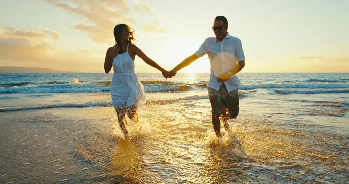 Happy couple in love, playing on the beach at sunset, running and splashing in the waves, travel vacation lifestyle.