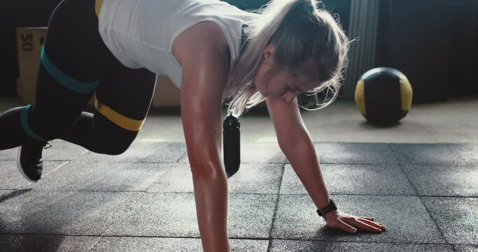 Fitness mobile app. Beautiful sporty athletic woman sets timer on smart watch doing leg exercises at modern light gym.