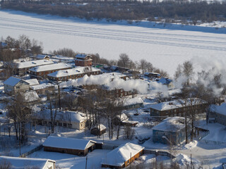 A suburb, village or industrial quarter of a winter city from a bird's-eye view (photo from an aerial drone). Russian backwoods, view on the frozen ice of the river Vyatka.