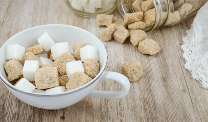 A white teacup, and pair of open glass jars filled with sugar cubes, raw sugar spilling out

