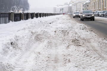 Uncleaned street with heavy snowdrifts after snowfall in the city, cars on the road on background. Winter bad weather. 