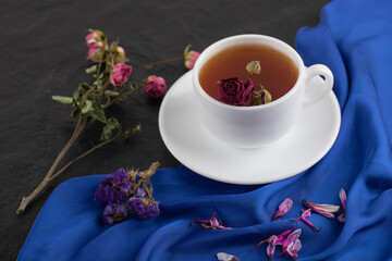 Dried roses with a cup of hot tea on a black background