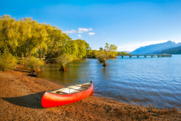 A red canoe on the shore of Lake Wakatipu at Glenorchy Wharf at golden hour in New Zealand, South Island.
