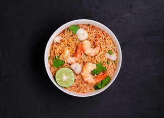 Ramen Instant Noodles in Spicy Shrimp Soup Tom Yum Kung - Asian style food. Placed on a black table with copy space, top view.