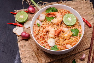 Ramen Instant Noodles in Spicy Shrimp Soup Tom Yum Kung - Asian style food. Placed on a black table with copy space, top view.