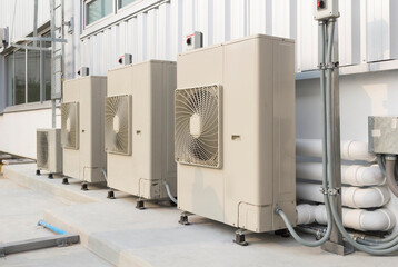 Condenser unit or compressor outside industrial plant building. Unit of central air conditioner (AC) or heating ventilation air conditioning system (HVAC). Electric fan and refrigerant pump inside.