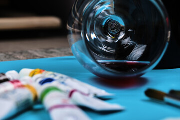 Colorful oil painting tubes, brushes and a glass of wine on dark table