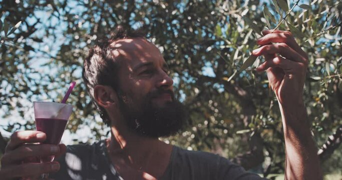 Man with beard sitting under a tree and drinking a bevarage 