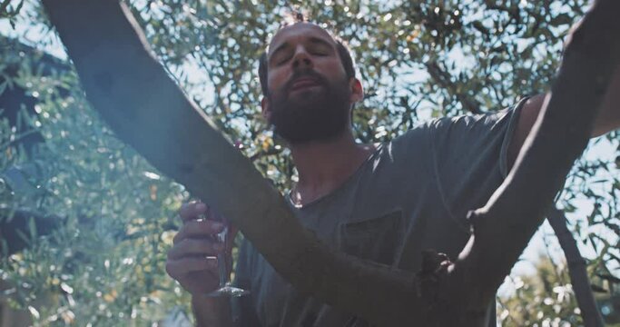 Man with beard sitting under a tree and drinking a bevarage 