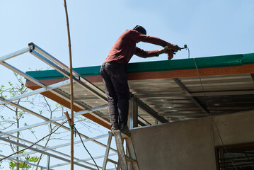 Unsafe Male Roofer Workman Using Electric Screwdriver Install Tile on Roof of New House in the Construction Site with no Protection.