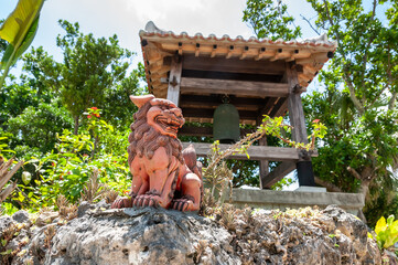Shisa, a traditional decoration from the Ryukyu Kingdom, Okinawa used for protection and behind it the traditional Japanese temple bell. Taketomi Island.