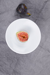 A plate of sliced fig and whole black fig on grey background
