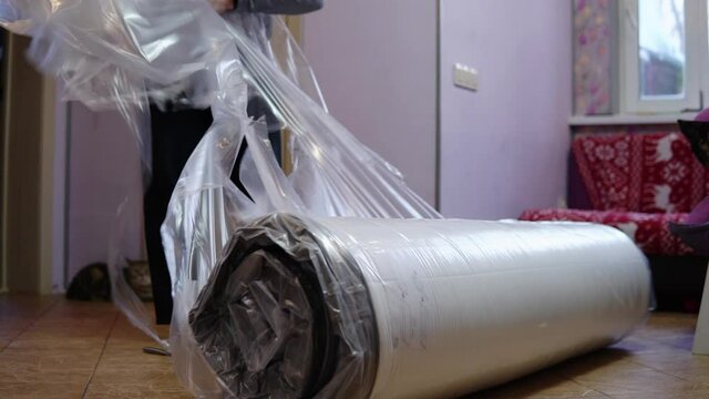 A grown man unpacks a new mattress. Unpacking the mattress with a knife pressed into the bag