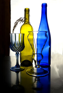 Bottles and wine glasses made of colored glass on a light background, selective focus