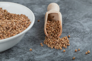 Pile of raw buckwheat on white plate with spoon