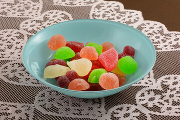 Summer fruit pear, apricot, green apple peach and watermelon juice filled gummy candy jellies in blue bowl on lace table runner on tablecloth