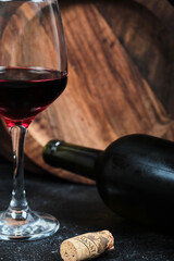 Bottle of wine with glass of wine on dark background with wooden plate