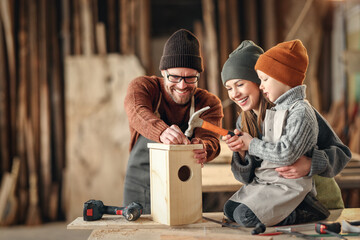 Kid with parents assembling wooden bird house in craft workshop