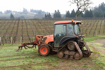 Obraz premium A vineyard worker is operating a row sweeper machine in the winter season in the rolling hills south of Salem, Oregon