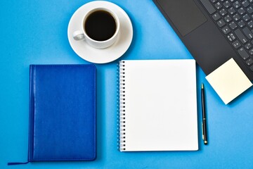 Blank notepad with laptop computer and cup coffee on blue background. Top view with copy space, flat lay and work from home concept.