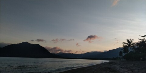 the sun sets on the beach among the mountains