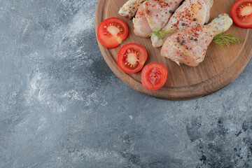 Raw chicken drumstick and organic tomato on wooden board