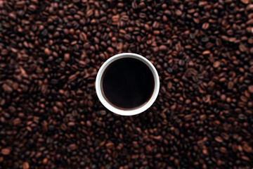 White cup of coffee on a bunch of roasted coffee beans background