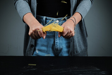 Woman breaking raw spaghetti on dark table
