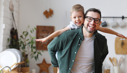 Joyful father piggybacking happy son in kitchen