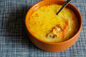 Cabbage soup with mixed sour cream and a metal spoon in a brown earthenware bowl.