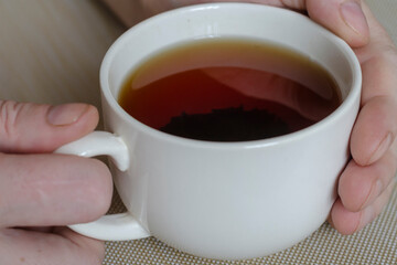 Close-up of male hands and a mug with tea on a beige surface.