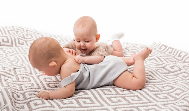 Funny babies playing together on floor at home or nursery. Kids have fun on the rug. Brother and sister. Dressed in cute knitted clothes