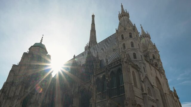 Cinematic view of St. Stephen's Cathedral in downtown of Vienna, Austria. Rays of sun between towers and tops of church. Bright sunny sky. Medieval Roman Catholic place of worship. Scenic panoramic.