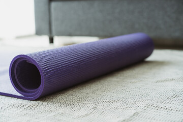 Rolled purple yoga exercise mat on the floor in living room close up with copyspace. Indoor workout activity concept. Rolling Purple Yoga carpet close up. © DG PhotoStock