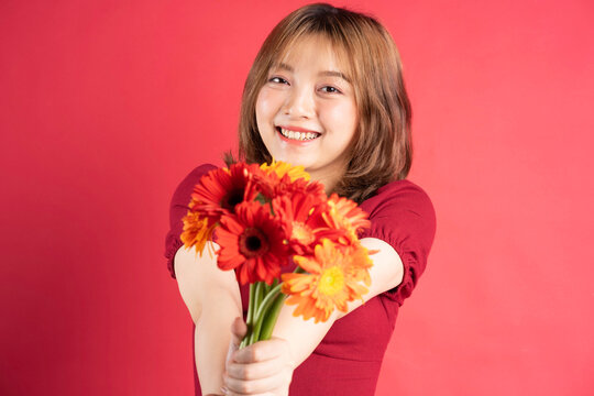 Young girl holding bouquet of gerberas with cheerful expression on background