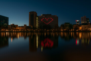 Fototapeta na wymiar City lights heart shaped on hotel building reflected on the river covid solidarity 