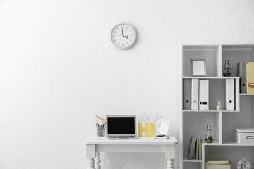 Modern comfortable workplace with laptop near light wall in office