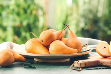 Plate with fresh ripe pears on table against blurred background