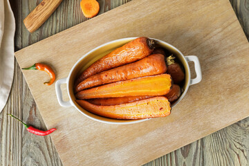 Dish of tasty baked carrot on wooden background