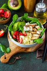 Healthy food, diet lunch menu concept, ketogenic diet and paleo diet. Couscous salad with strawberries, grilled chicken, avocado and feta cheese on a stone table. Copy space.