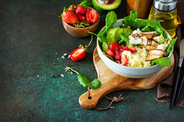 Healthy food, diet lunch menu concept, ketogenic diet and paleo diet. Couscous salad with strawberries, grilled chicken, avocado and feta cheese on a stone table.