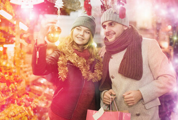 Obraz na płótnie Canvas Smiling girl with boy choosing decorations at Christmas market