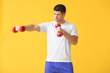 Sporty young man training with dumbbells on color background