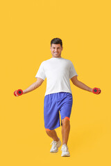 Funny young man training with dumbbells on color background