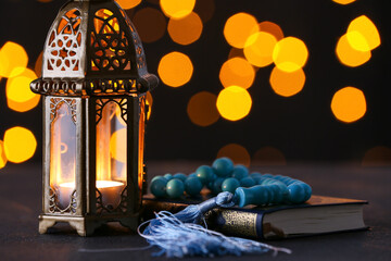 Muslim lamp, tasbih and Koran on dark background with blurred lights