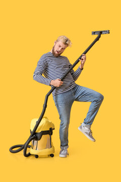 Young man with vacuum cleaner having fun on color background