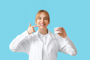 Female dentist with plastic jaw model on color background