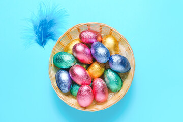 Wicker bowl with sweet chocolate eggs on color background