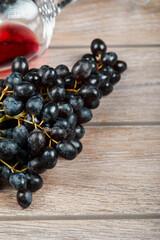 A bunch of black grapes and a glass of wine on wooden background